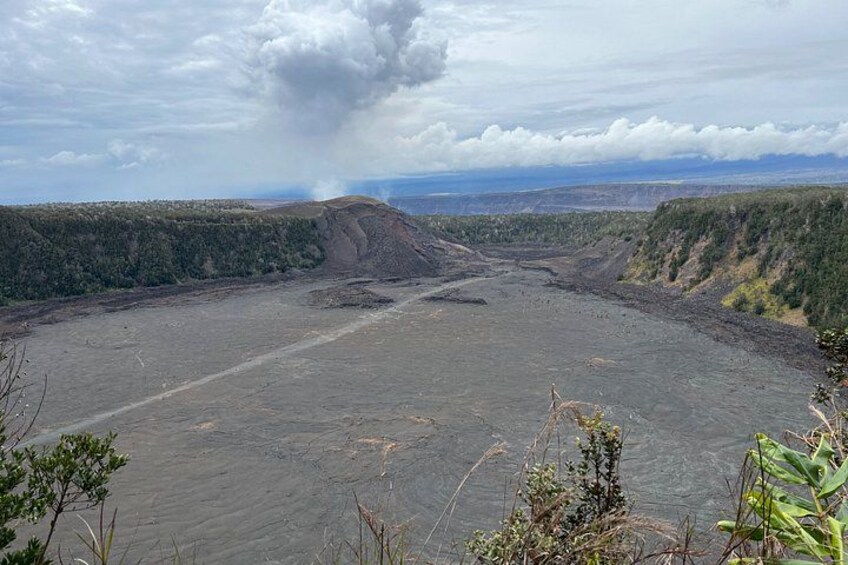 A volcanic crater with a plume of smoke, surrounded by forested hills. 5