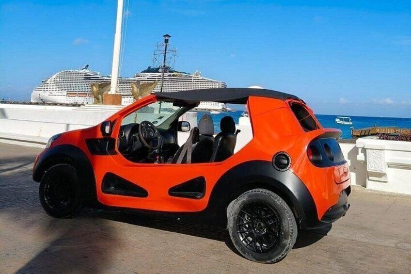 Un coche rojo y negro estacionado en una carretera costera, con un crucero al fondo. 2