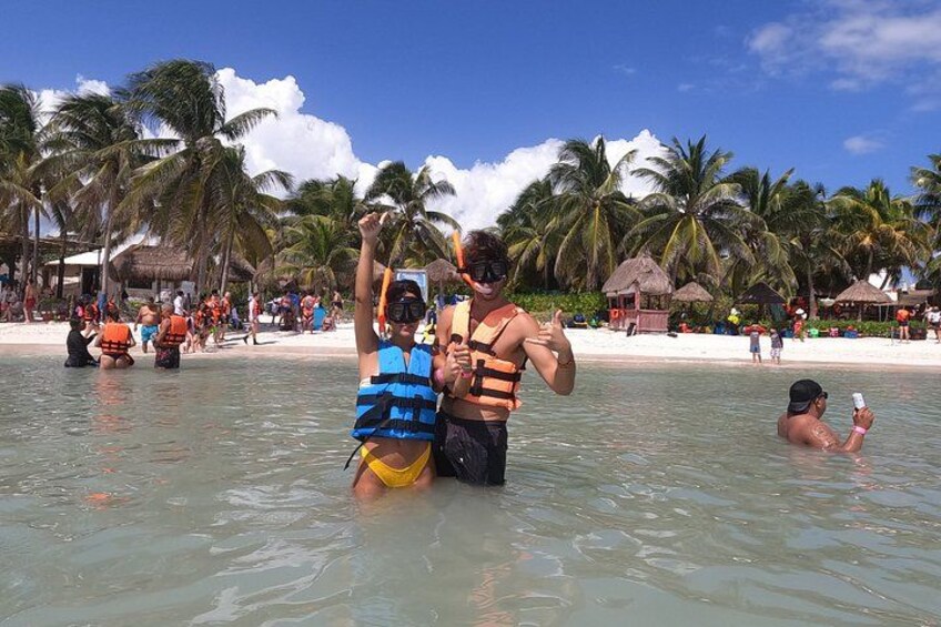 A beach with people in the water, palm trees, and thatched-roof huts. 3