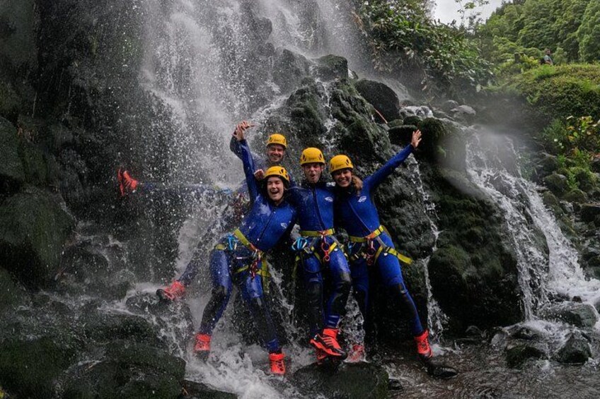 Three people in blue wetsuits and yellow helmets posing in front of a waterfall. 2