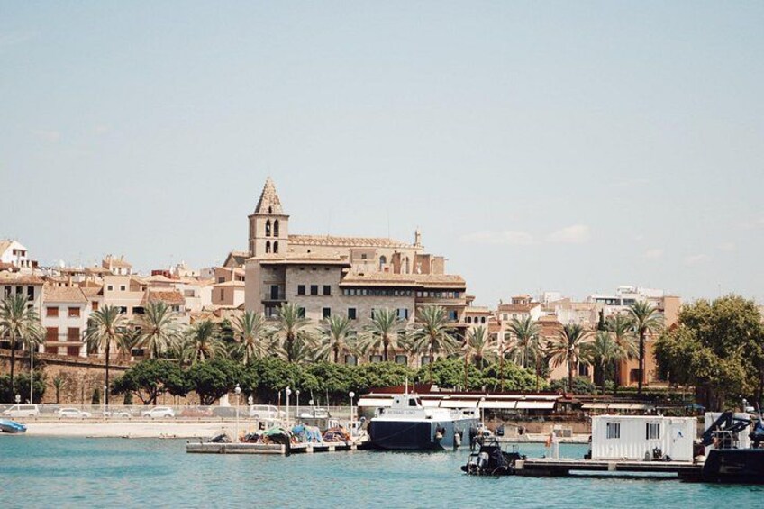 Un paisaje urbano costero con un edificio destacado que tiene una torre, palmeras y barcos en el agua. 5