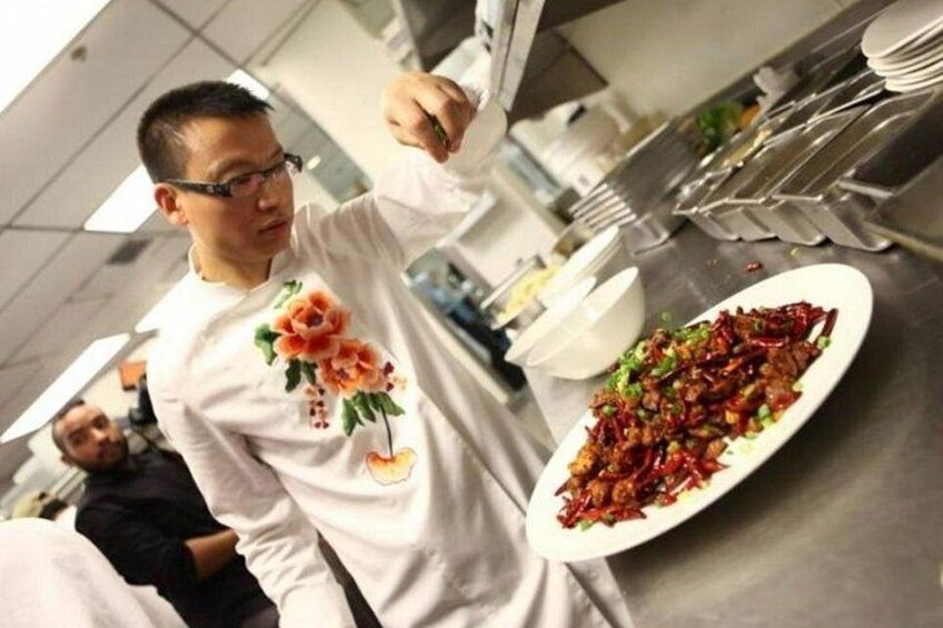 Une personne portant une chemise blanche ornée de broderies florales, en train de servir un plat de légumes saut és. 1