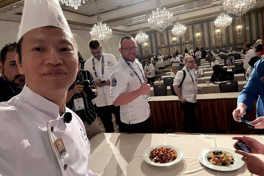 Un événement formel où les participants sont vêtus de blanc, avec une table dressée et des lustres en arrière-plan. 3