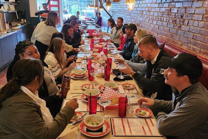 A group of people dining at a long table in a restaurant with brick walls and hanging lights. 2
