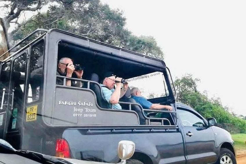 A safari vehicle with passengers, a Jeep Tour sign, and a partial view of a vehicle in the foreground. 5