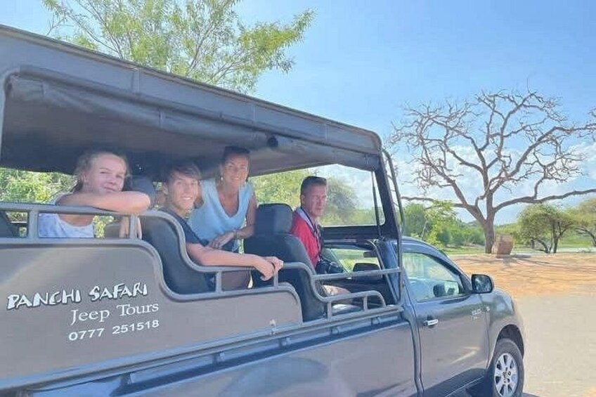 A safari vehicle with people inside, a tree, and a clear sky. 4