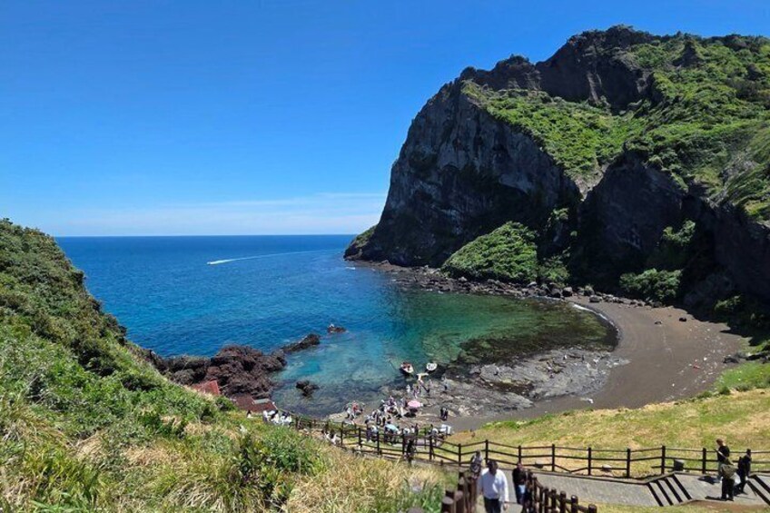 A coastal landscape with a clear blue sea, rocky cliffs, and a sandy beach. 5
