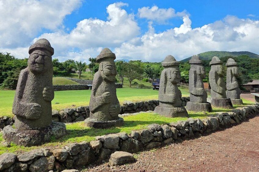 A row of stone statues in a grassy area with a stone wall and a mountain in the background. 5