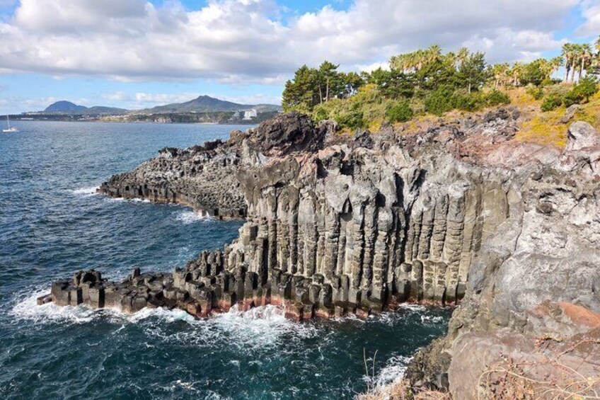 A coastal cliff with vertical rock formations, a body of water, and distant mountains. 2