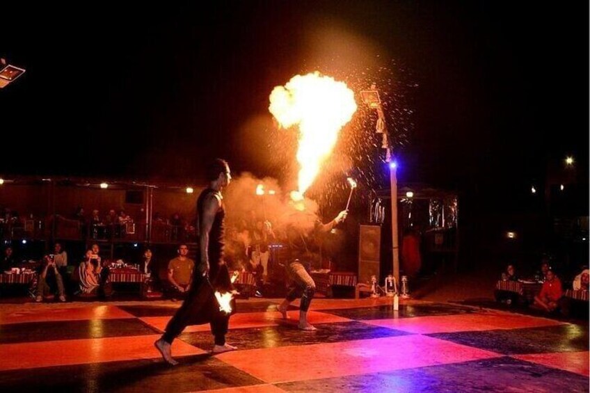 A person performing with a fire act, a crowd watching, and a stage with tables and chairs. 2