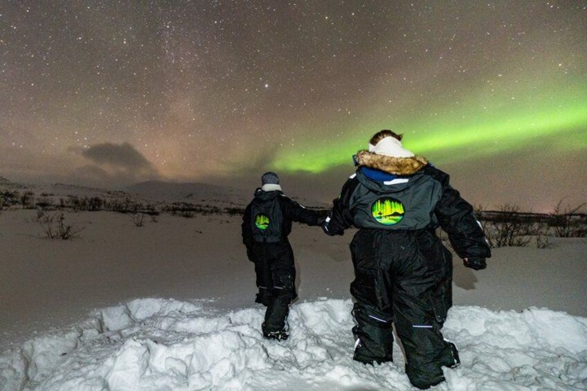 Two people walking on snow with the aurora borealis in the background. 4