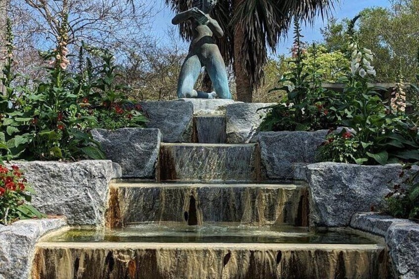 Una fuente de piedra con una estatua de una figura, rodeada de rocas y plantas. 3