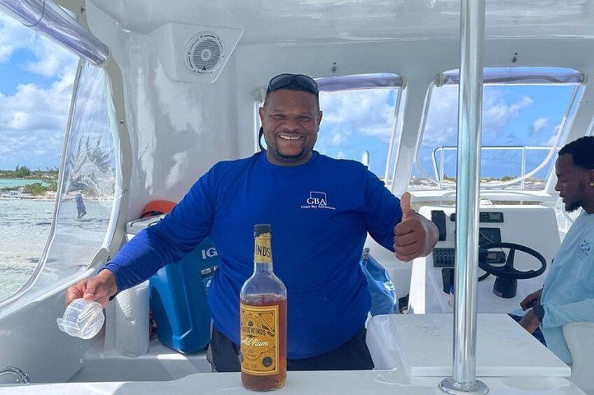 A person on a boat with a bottle of rum, a steering wheel, and a clear sky. 5