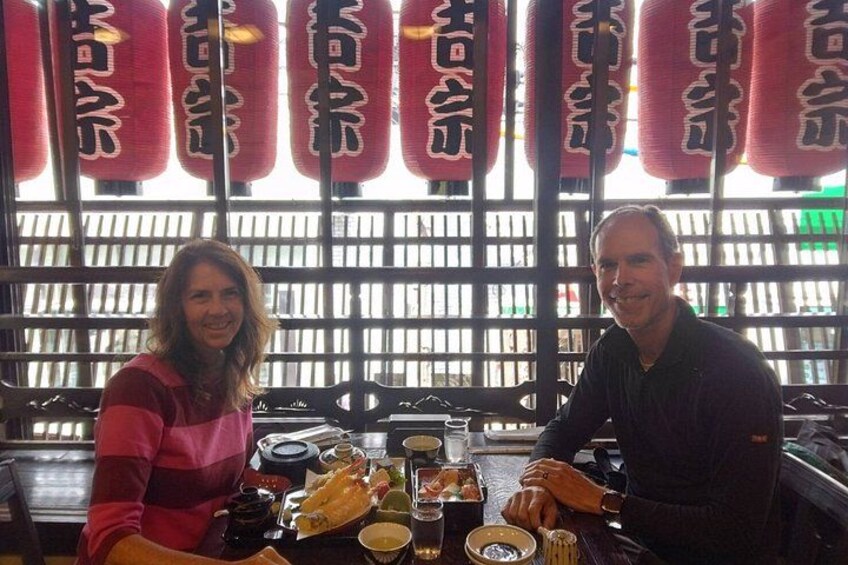 Two people sitting at a table with food and drinks in a restaurant with red lanterns in the background. 5