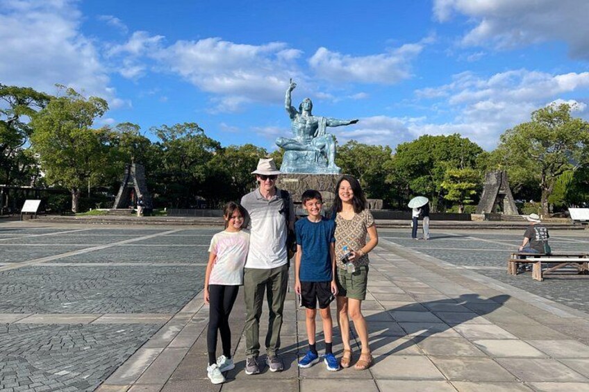 A family posing in front of a statue in a park with trees and a clear sky. 3