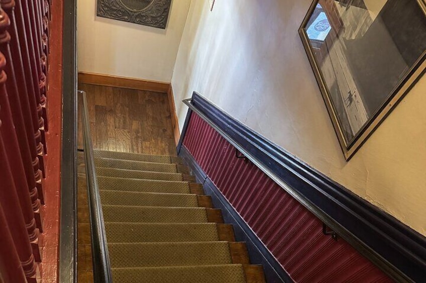 Una scala con gradini in legno e ringhiere rosse, che conduce a un pianerottolo con un quadro incorniciato appeso al muro. 4