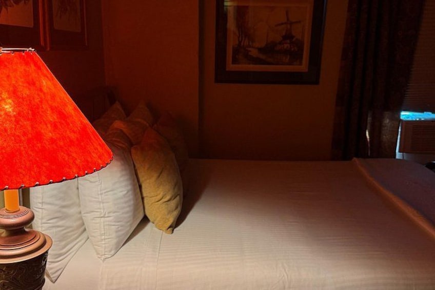Un letto con lenzuola bianche, una lampada rossa e un quadro appeso al muro. 3