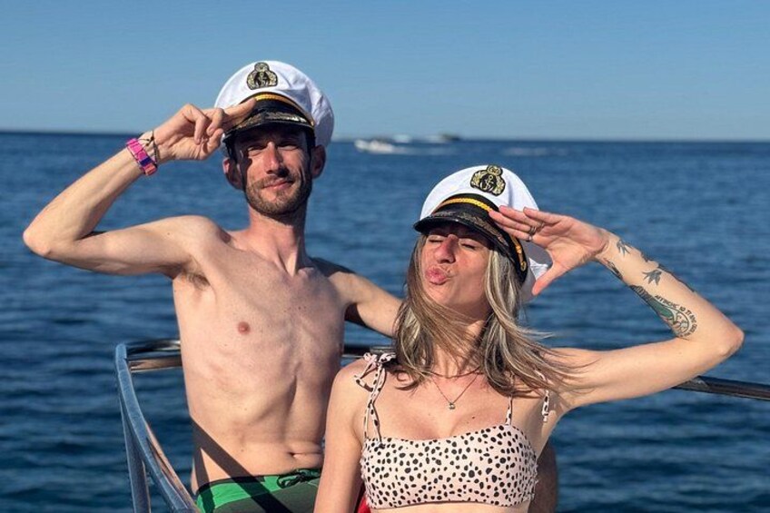 Deux personnes à bord d’un bateau, portant des chapeaux de marin, avec l’océan et un ciel dégagé en arrière-plan. 4