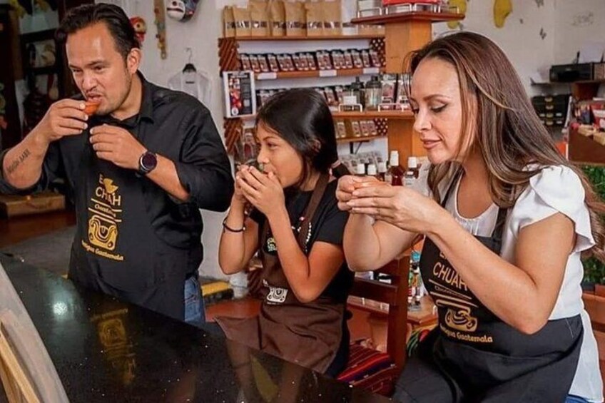 Three people wearing aprons in a kitchen setting with shelves of spices and condiments in the background. 2