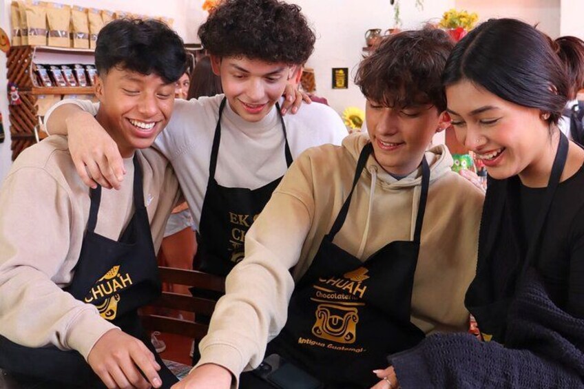 Four people wearing aprons with a logo, sitting closely together. 1