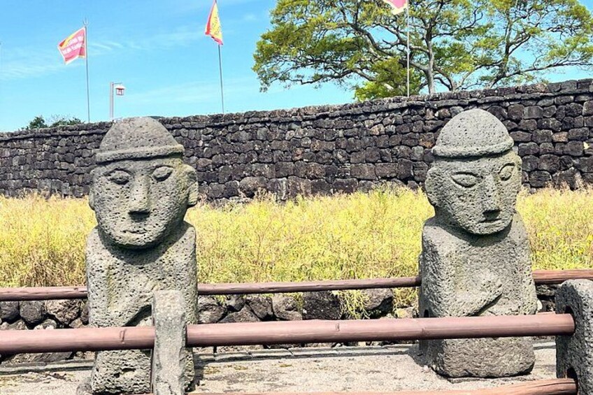 Dos estatuas de piedra con sombreros, un muro de piedra y banderas al fondo. 5