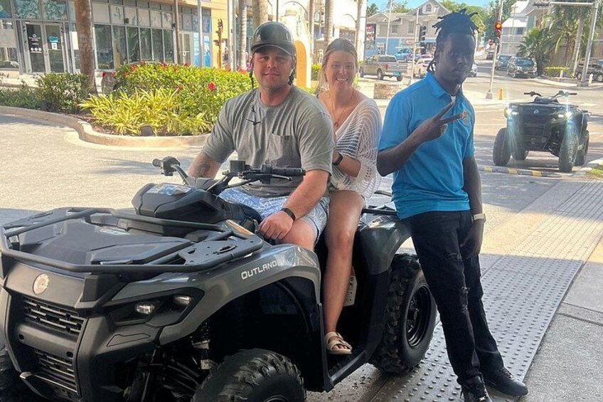 A quad bike with OUTLAND brand on the front, a person standing beside it, and another person sitting on it. 2