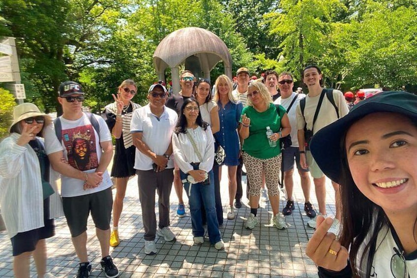 Eine Gruppe von Menschen steht in einem Park mit Bäumen und einer Laube im Hintergrund. 4