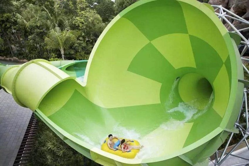 A large green water slide with a person and a child at the bottom. 2