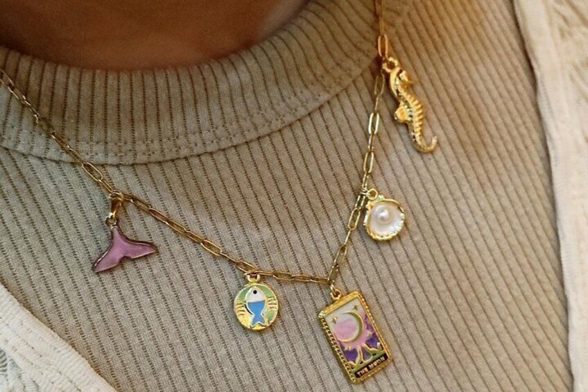 En person iført en beige ribstrikket sweater og et guldhalskæde med charms. 3
