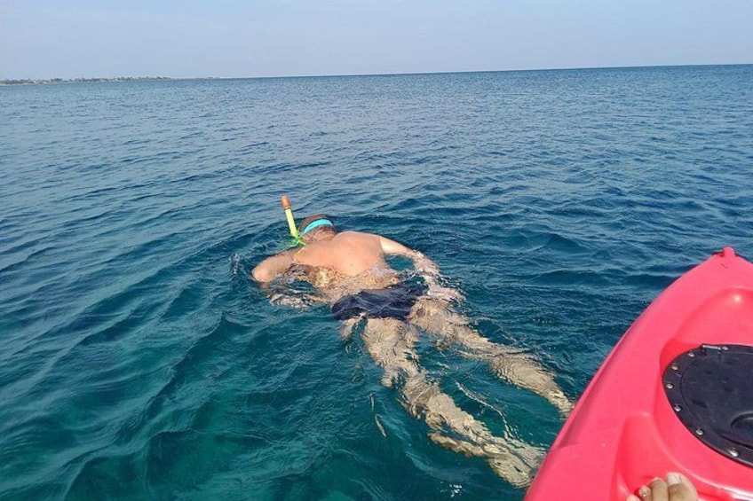 A person floating in the water with a snorkel, a red kayak nearby, and a calm sea. 2