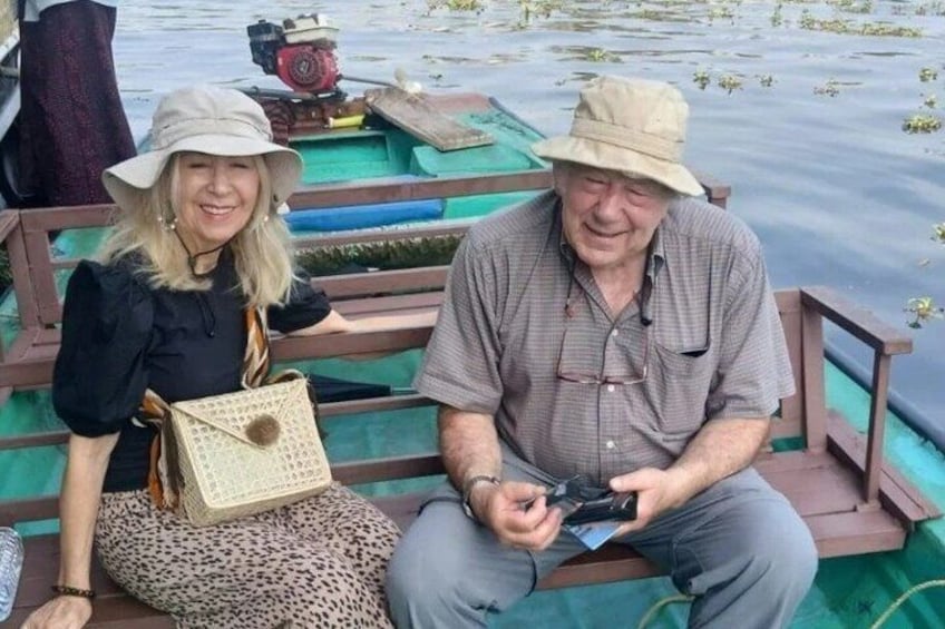 Two people sitting on a bench by a body of water with a boat in the background. 5