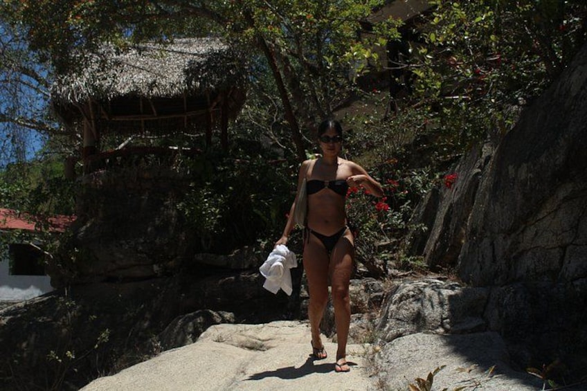 A person in a bikini walking on a rocky path with a thatched-roof structure in the background. 4