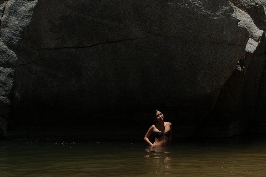 A person sitting in a body of water with a large rock formation in the background. 2