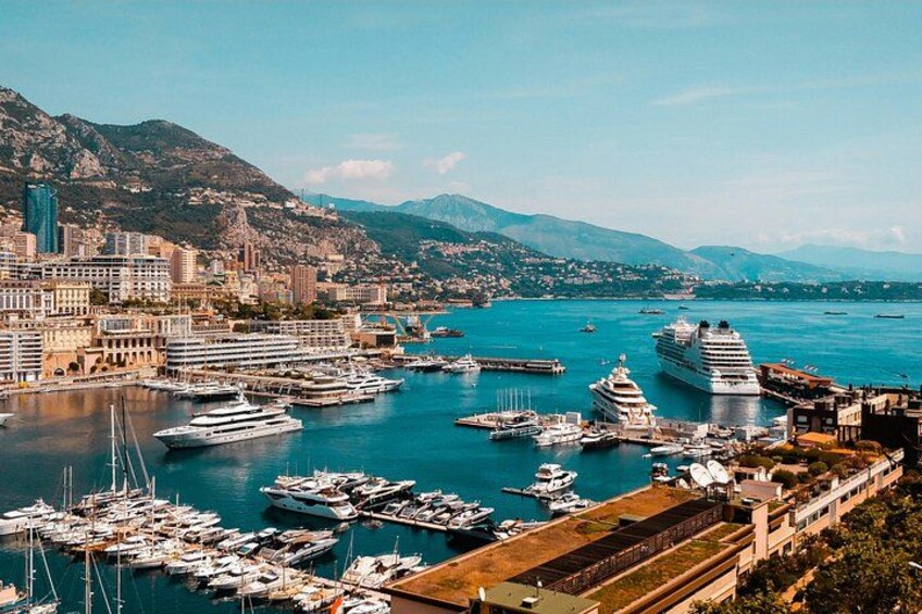 Een kustplaats met een jachthaven vol jachten en cruiseschepen, omringd door bergen en stadsgebouwen. 5