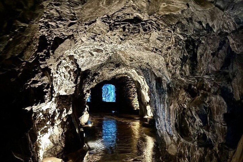 Una cueva con un curso de agua, paredes rocosas y un túnel iluminado en azul. 2