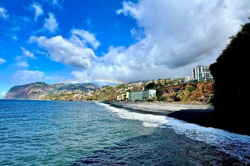 Un paisaje costero con playa, olas oceánicas, una montaña y edificios. 4