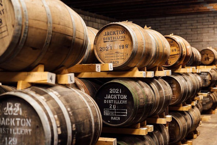 Reihenweise gestapelte Holzfässer, jedes mit dem Aufdruck 'Jackton Distillery 2021'. 2