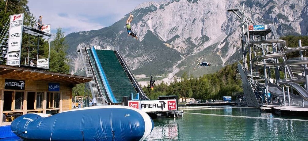 A water slide with a person mid-air, a mountain in the background, and a building with 'SOLDEN' signage. 4