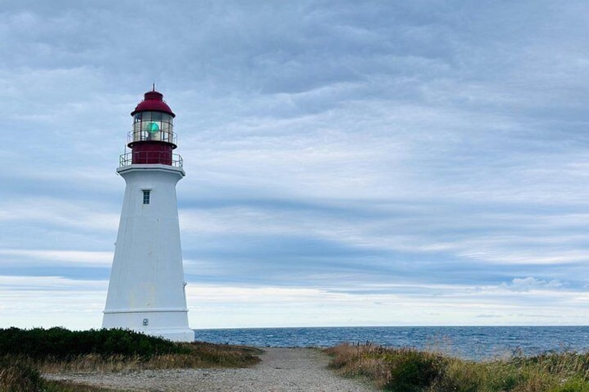 A white lighthouse with a red top, a gravel path leading to it, and the ocean in the background. 5