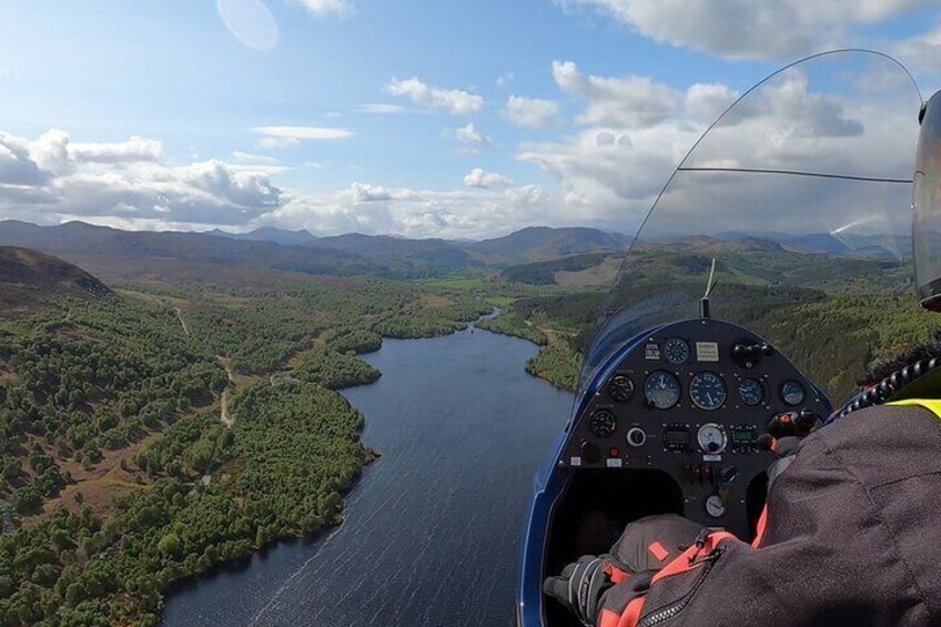 A helicopter cockpit with a view of a river surrounded by hills. 5