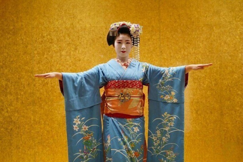 A person in traditional Japanese attire with a blue kimono and orange obi, standing with arms outstretched against a yellow background. 4