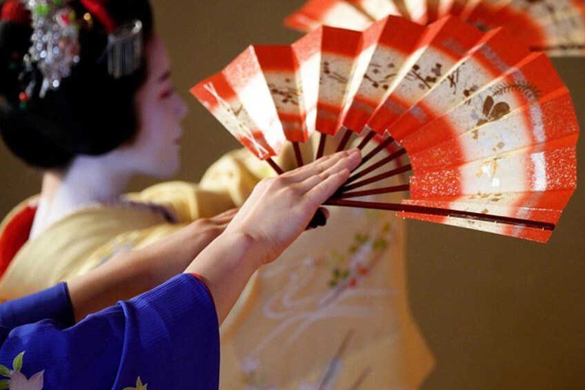 Una persona vestida con atuendo tradicional japonés sosteniendo un abanico con un diseño rojo y blanco. 4