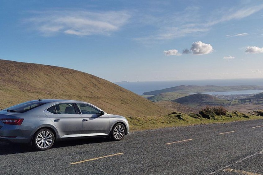 A silver car parked on a road with a hilly landscape in the background. 2