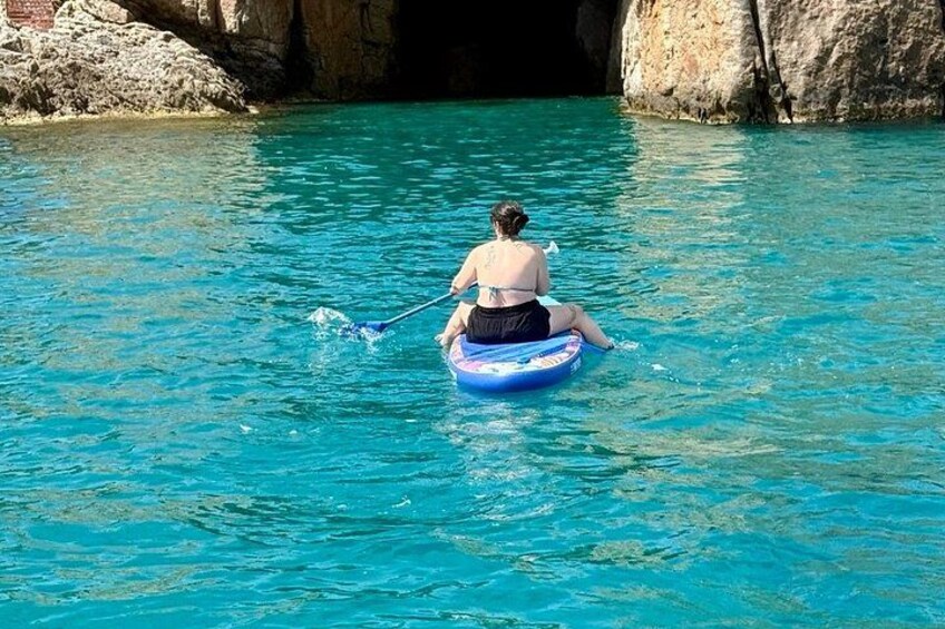 A person sitting on a blue raft in clear blue water, paddling with a stick. 5