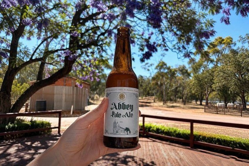 A bottle of Abbey Pale Ale held by a hand, with a park and trees in the background. 2