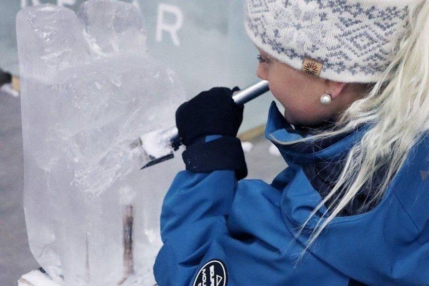 A person in a blue jacket and hat working on an ice sculpture. 1