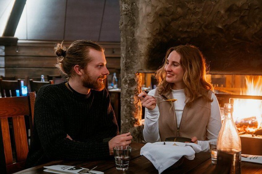 Two people sitting at a wooden table with a lit fireplace in the background. 4