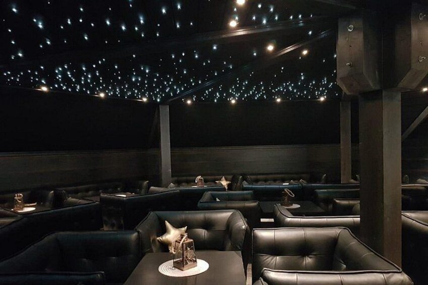 A dimly lit restaurant with leather booths and tables, starry ceiling lights, and a modern design. 2