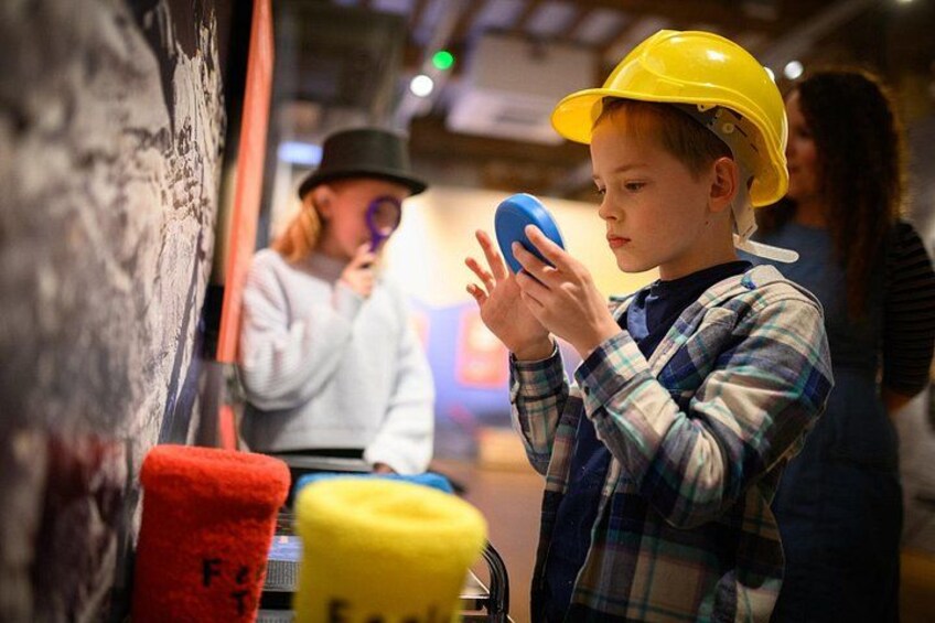 A child wearing a yellow hard hat holding a blue object, with red and yellow objects on the ground. 4