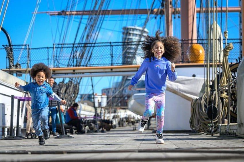 A child running on a wooden boardwalk with a large ship in the background. 1